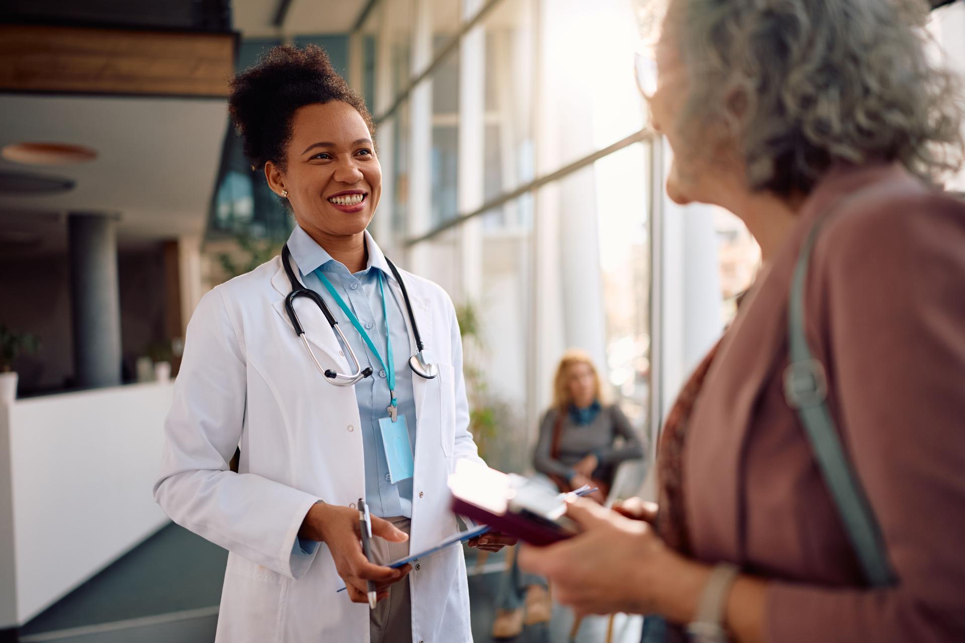 Happy black doctor talking to female senior patient at polyclinic